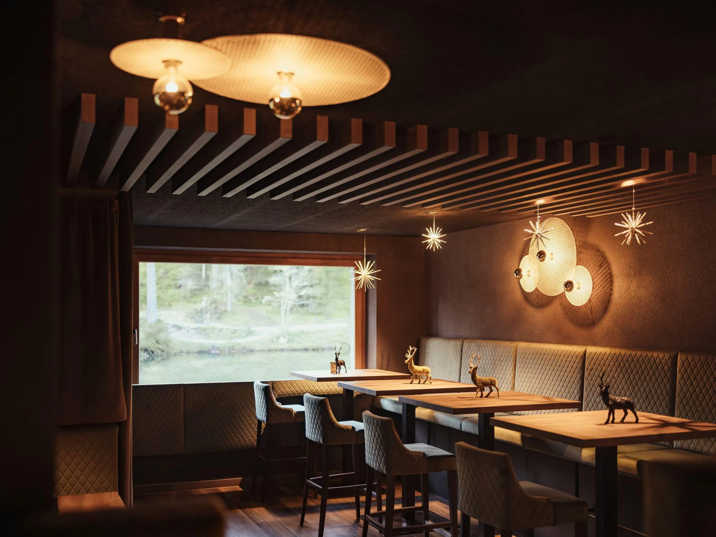 Accogliente sala da pranzo nell'Hotel Lech da Sompunt, La Villa, con illuminazione elegante, sedute morbide e piccole statuette decorative di cervi sui tavoli.