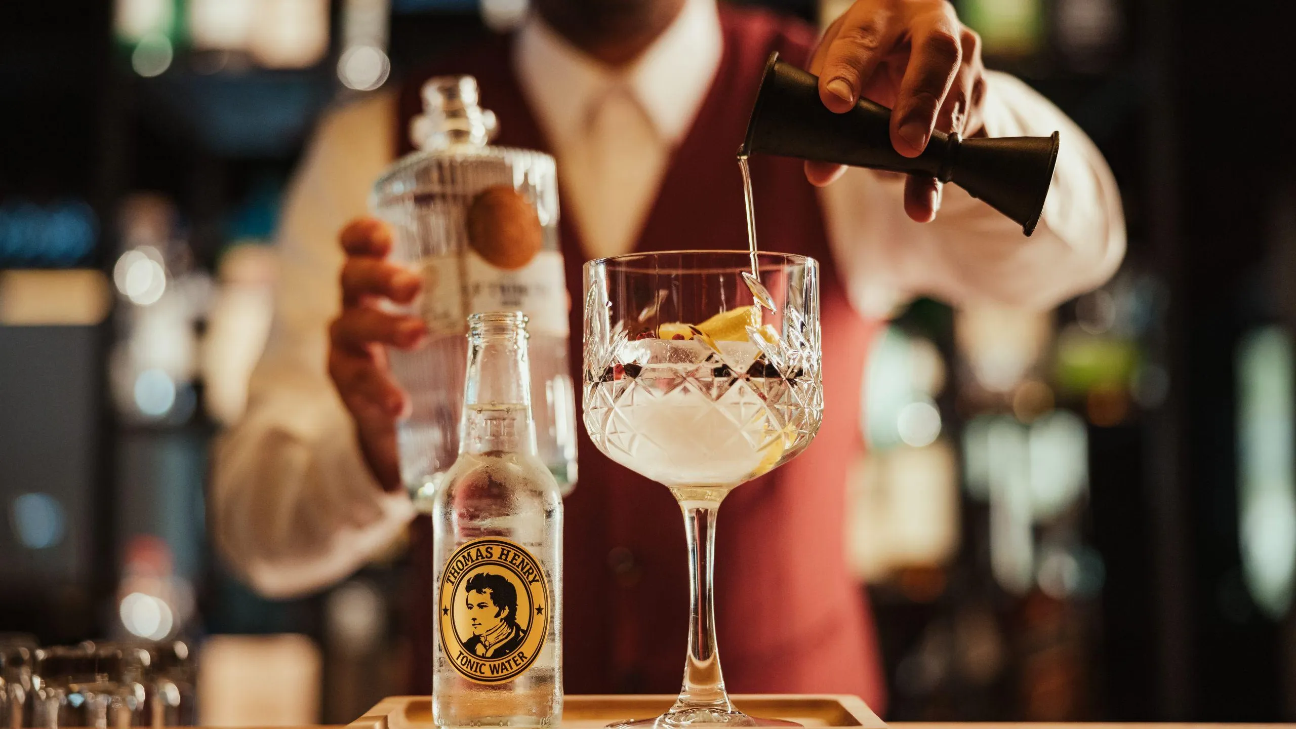 A bartender pours tonic water into a crystal glass filled with ice and lemon, showcasing a stylish cocktail preparation at Hotel Lech da Sompunt.