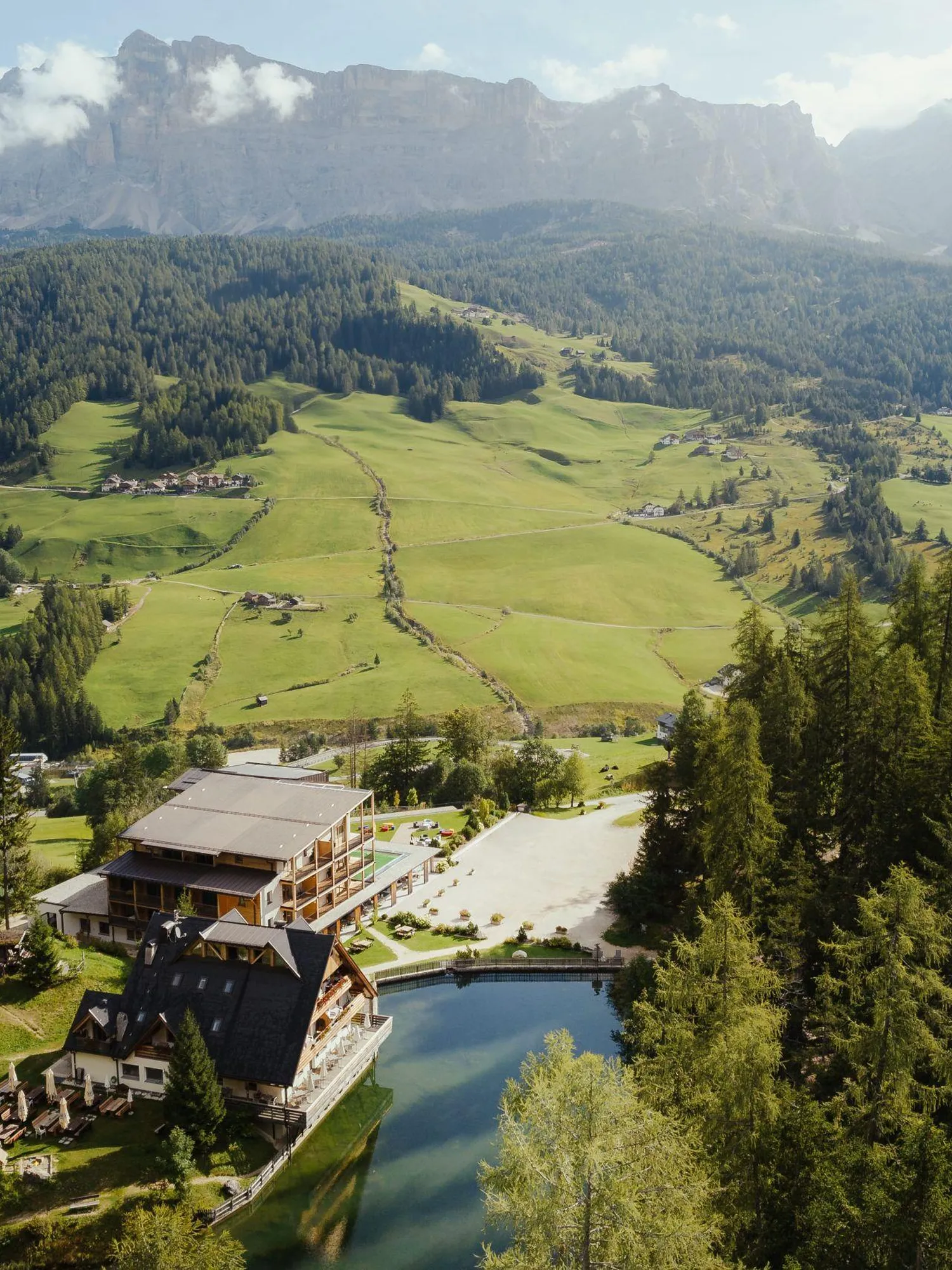 Panoramic Hotel Lech da Sompunt in La Villa, Alta Badia, nestled among lush green and mountains, with the beautiful lake Sompunt.