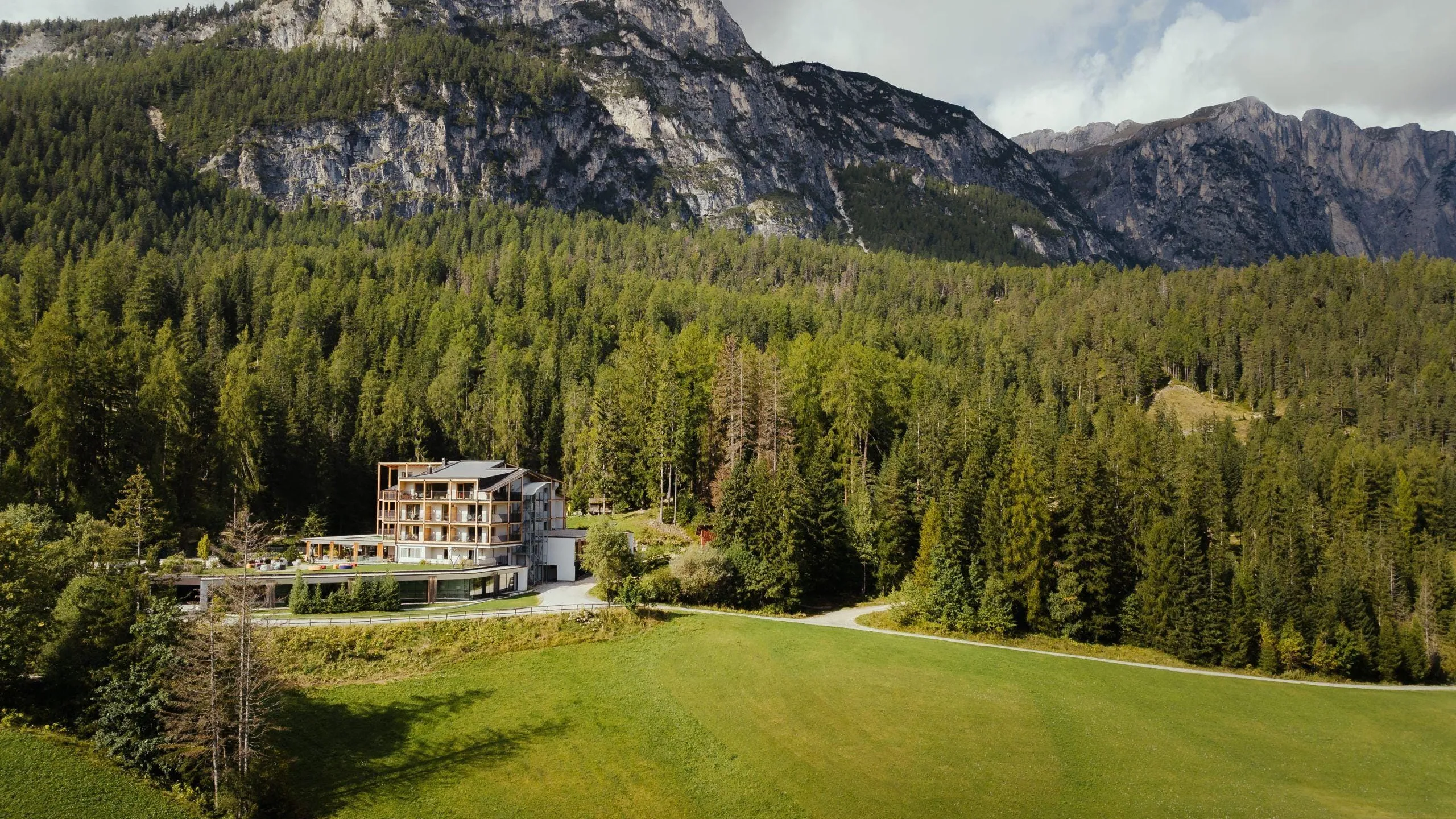 Hotel Lech da Sompunt nestled among lush trees, with the mountains of the Gardenacia in the background.