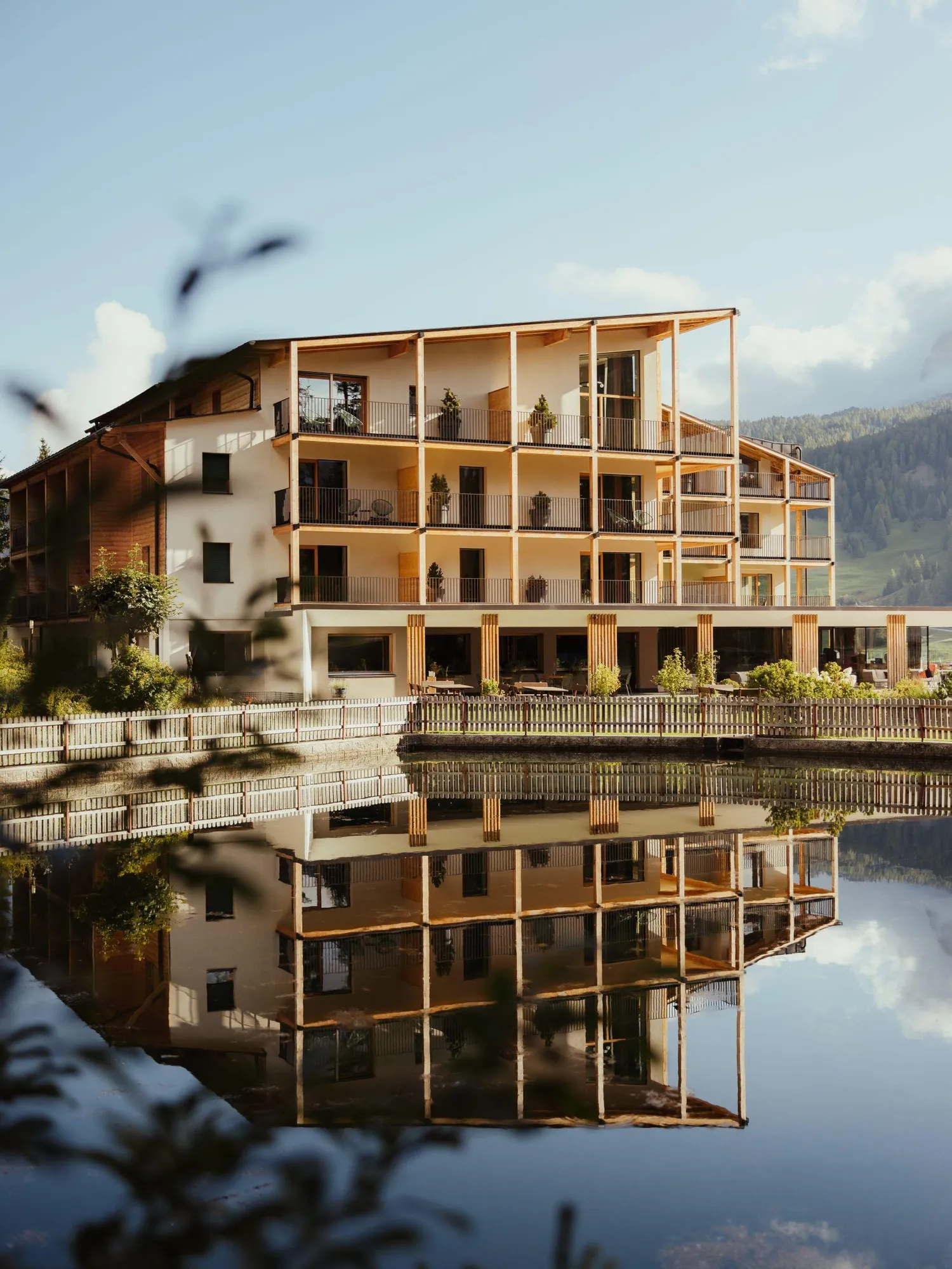 Hotel Lech da Sompunt in La Villa, Alta Badia, reflected in serene water.
