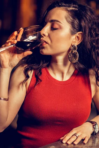 Una donna sorseggia con grazia del vino rosso, sfoggiando eleganti orecchini, immortalata nella calda atmosfera dell'Hotel Lech da Sompunt, La Villa.