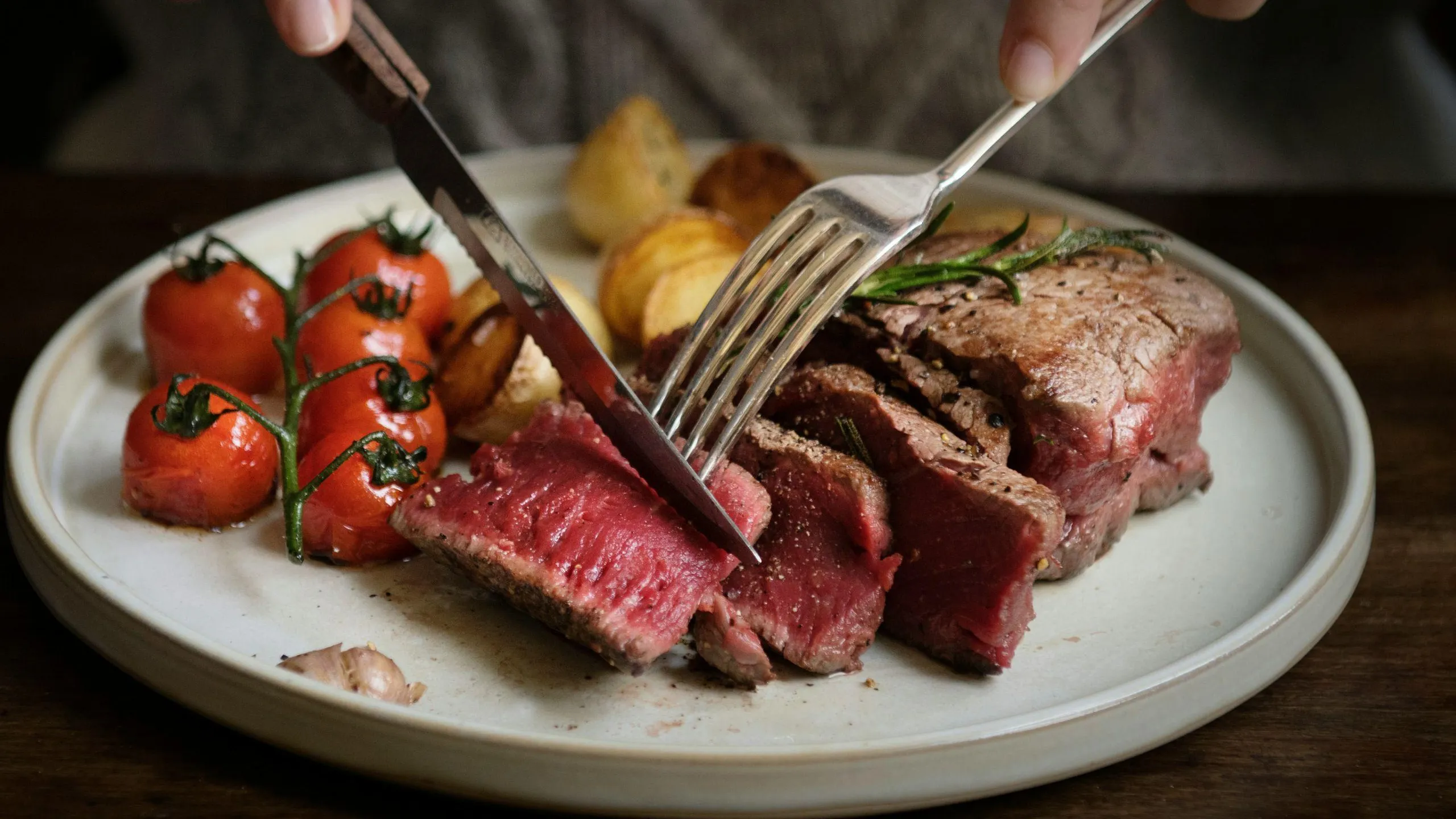 Un primo piano di un piatto con una tenera bistecca rossa tagliata a fette, accompagnata da pomodori arrostiti e patate, per un'esperienza culinaria da gourmet.