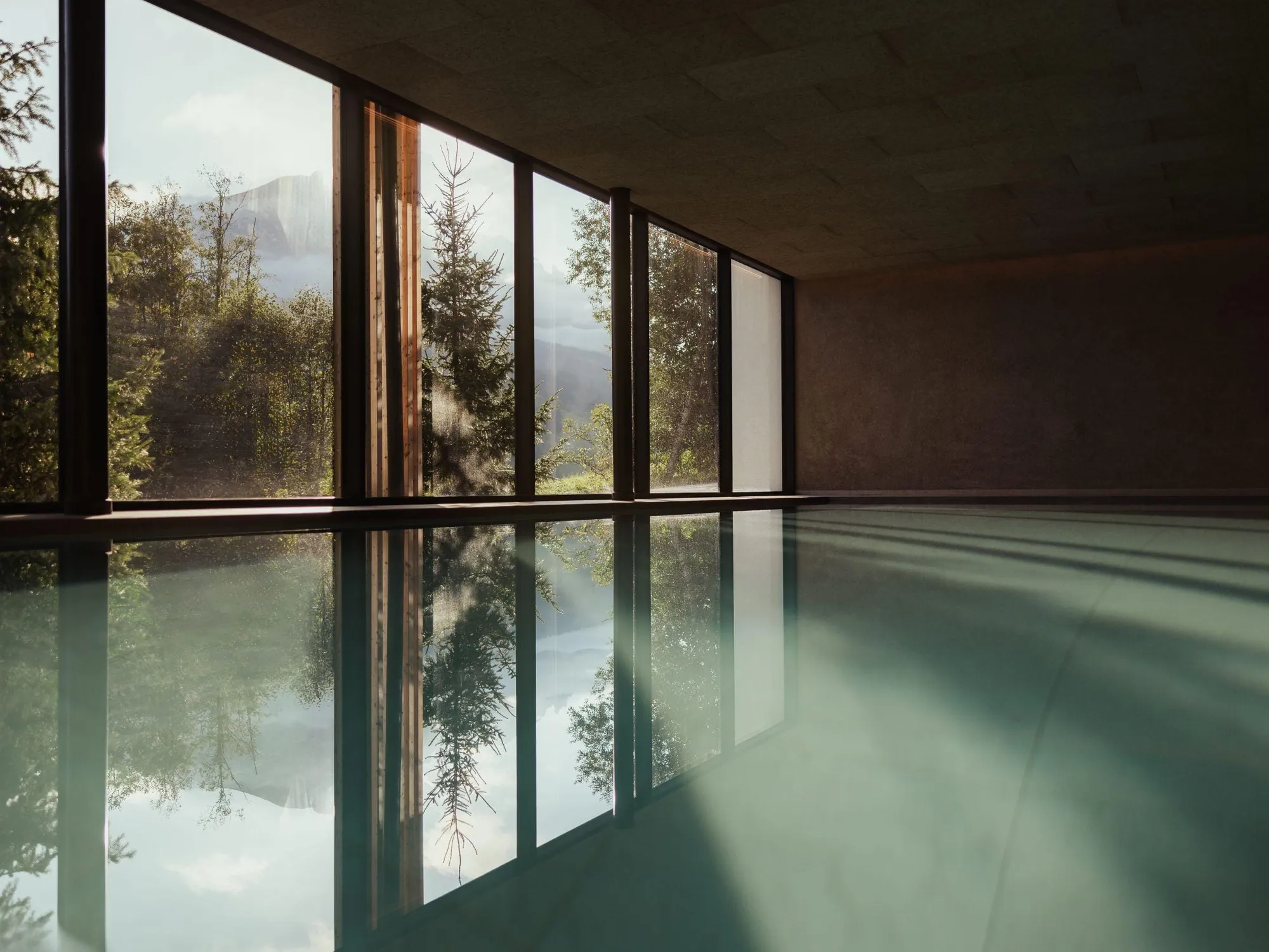 Piscina coperta presso l'Hotel Lech da Sompunt, con ampie vetrate che si affacciano sul verde lussureggiante e sulle Dolomiti, riflettendo una morbida luce naturale.