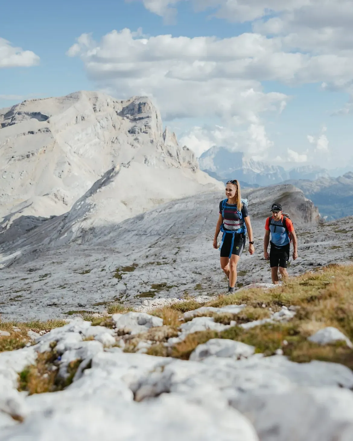 Due escursionisti percorrono il sentiero delle 4 cime in Alta Badia, circondati dalle imponenti e aspre vette delle Dolomiti.
