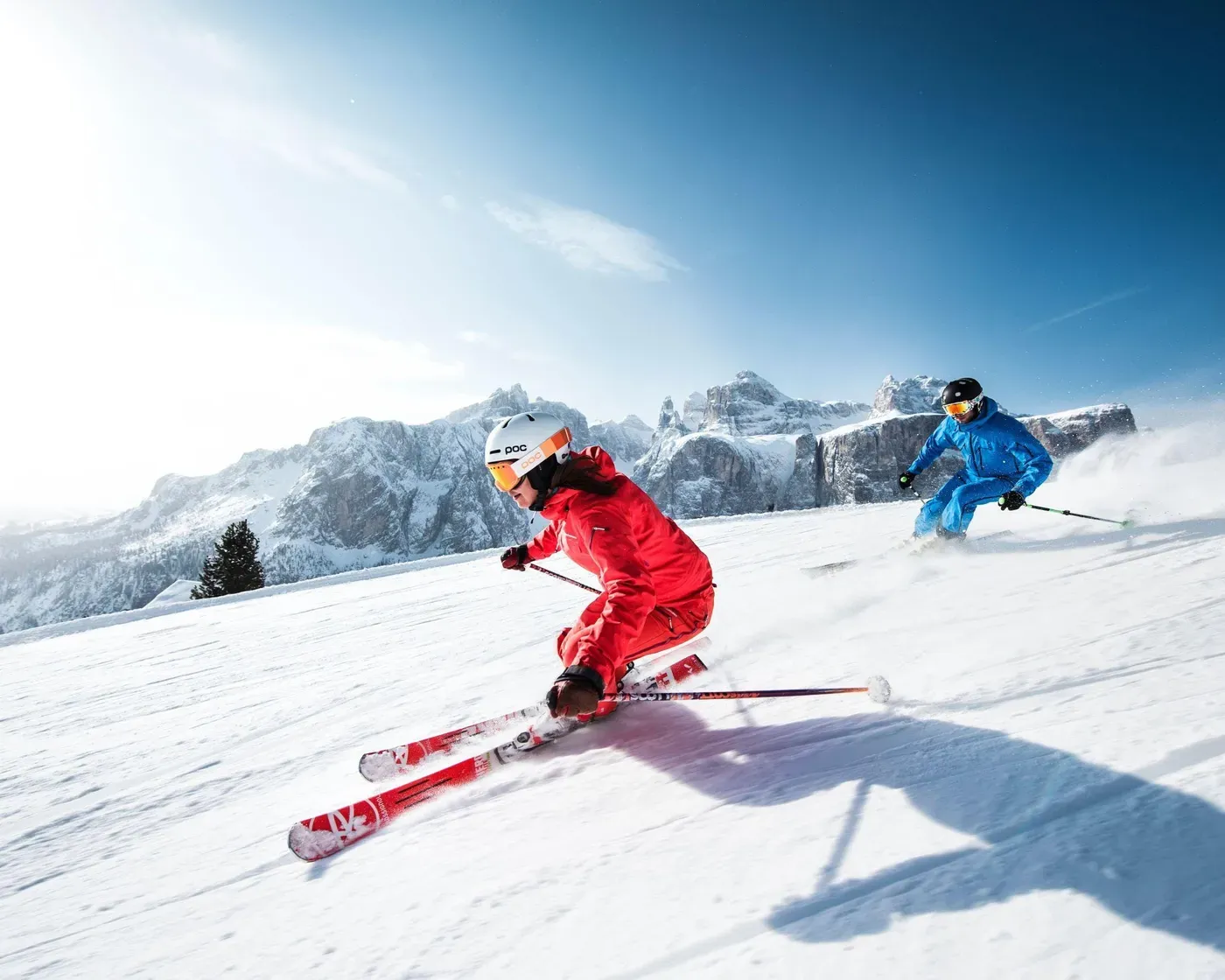 Due sciatori scendono a tutta velocità lungo un pendio innevato, sullo sfondo delle aspre montagne delle Dolomiti.