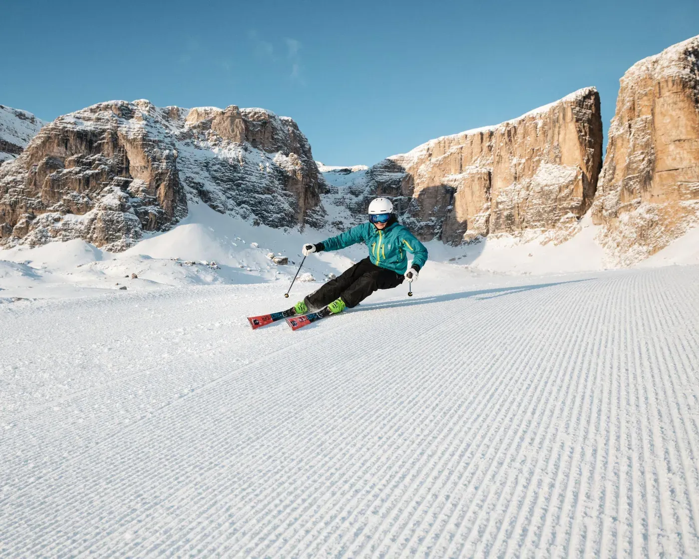 Uno sciatore con giacca blu e casco scende lungo la pista da sci di Valon nel Dolomiti Superski.