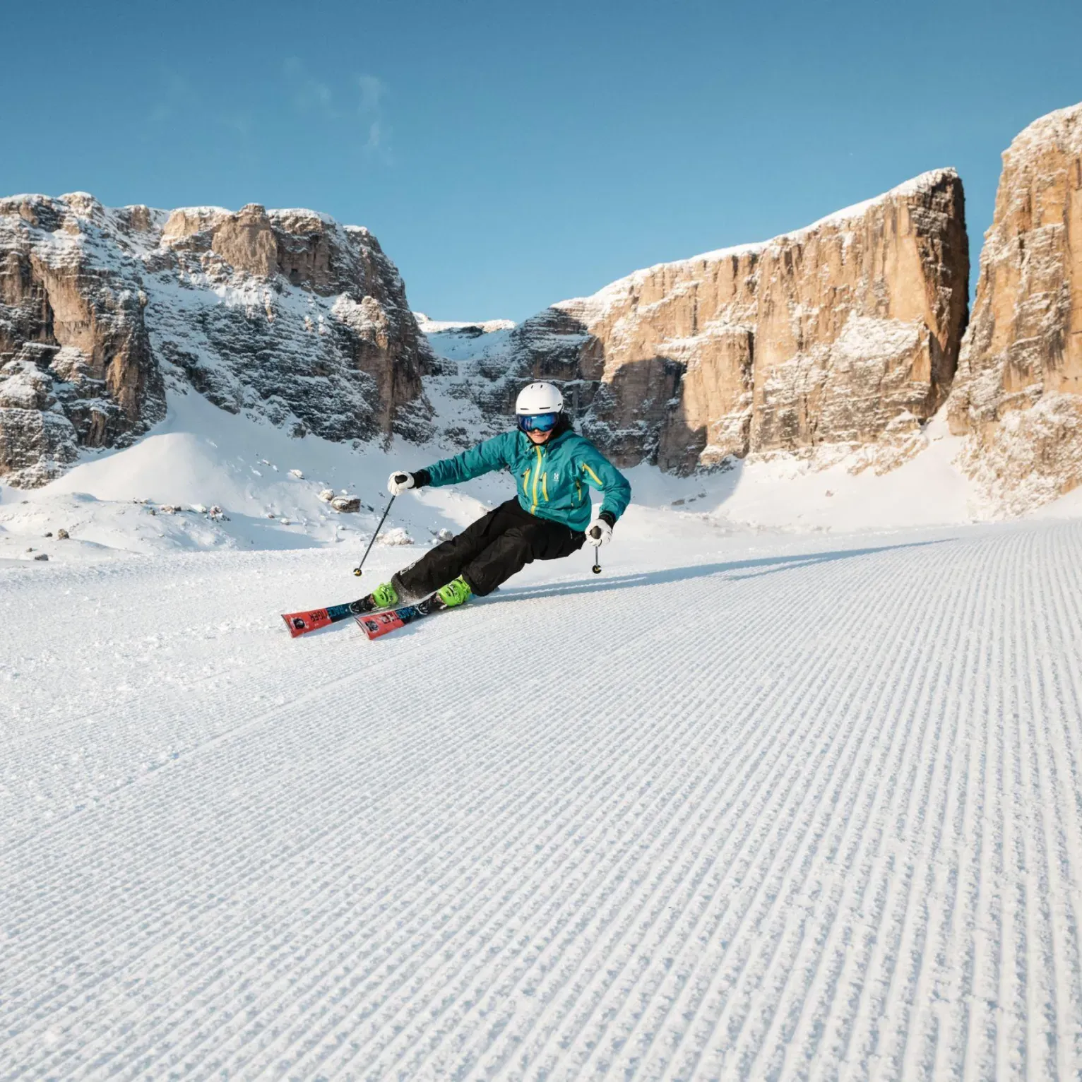 A skier in a blue jacket and helmet carves down the ski slope of Valon in the Dolomites Superski.