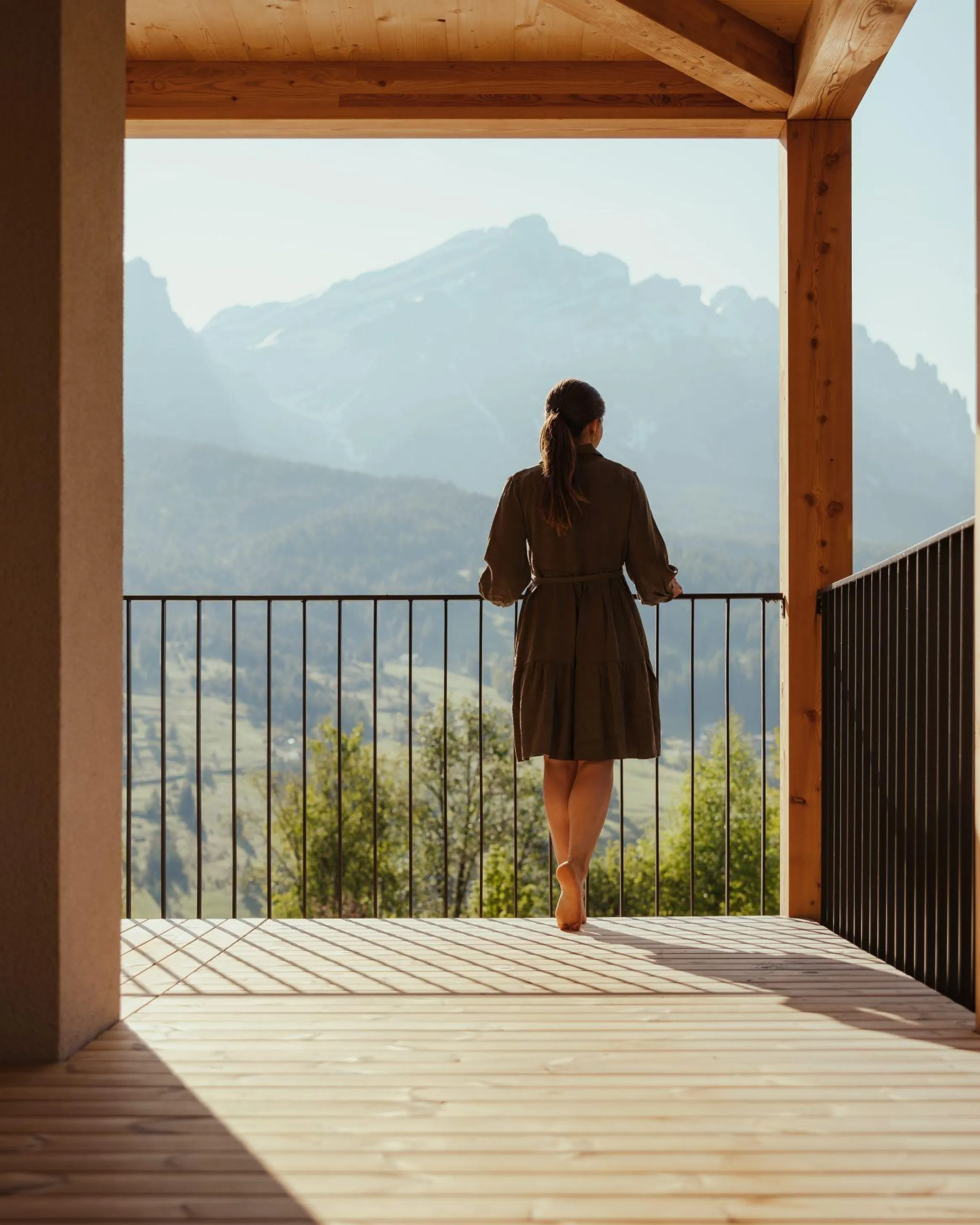 A woman stands on a wooden balcony of the Hotel Lech da Sompunt and looks at the distant mountain La Varella in Alta Badia.