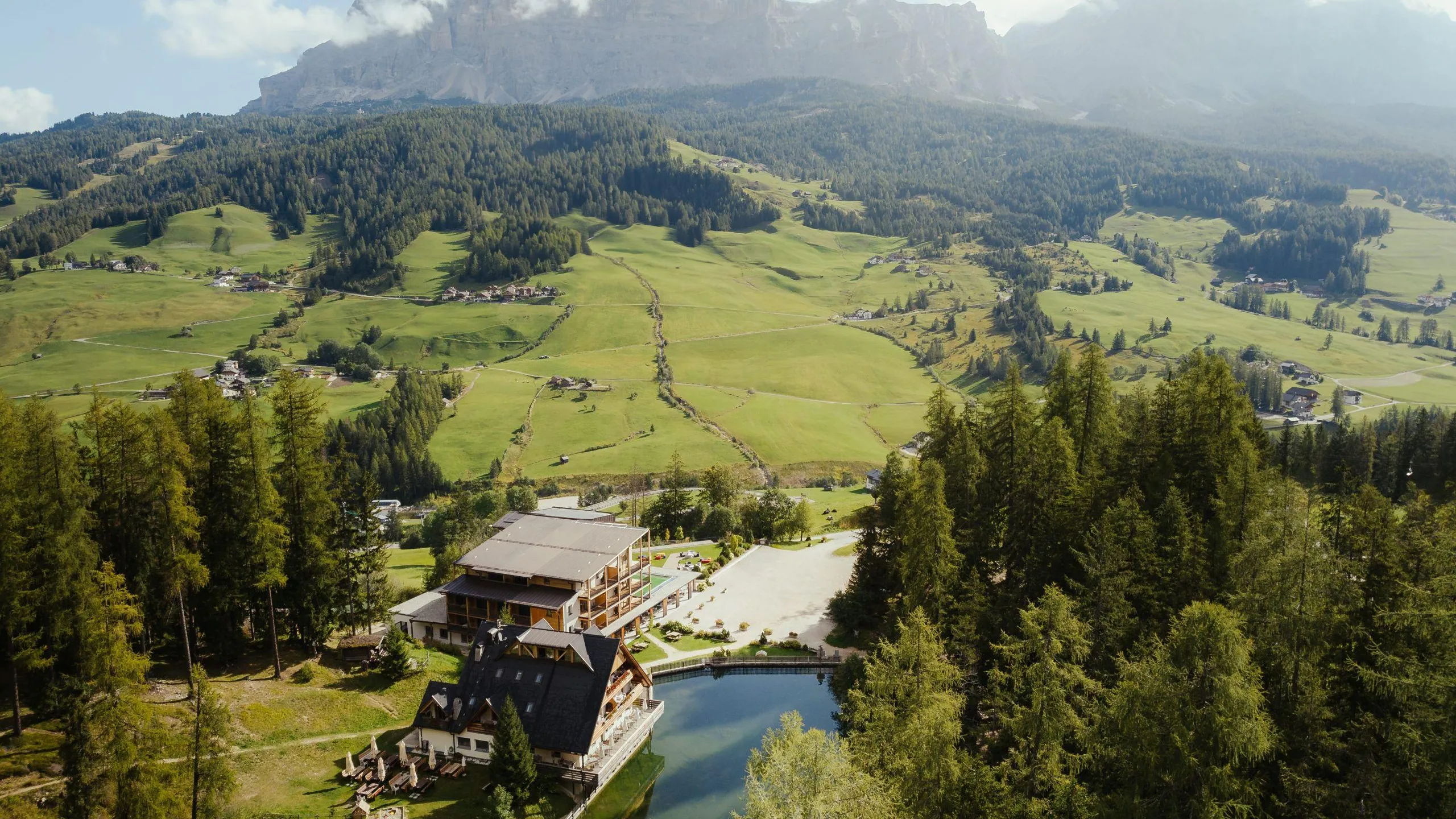 Panoramic Hotel Lech da Sompunt in La Villa, Alta Badia, nestled among lush green and mountains, with the beautiful lake Sompunt.