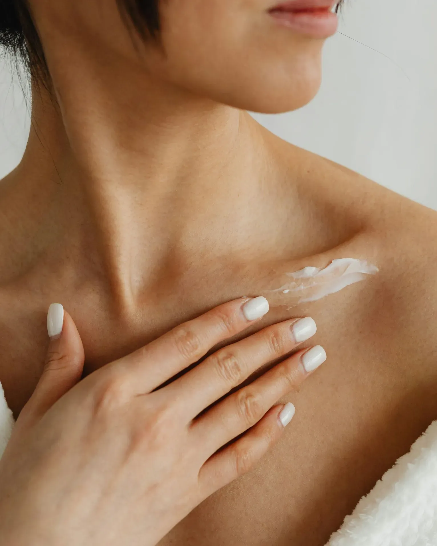 A close-up of a woman's shoulder and neck, gently applying cream with a soft hand. Spa Hotel Lech da Sompunt.