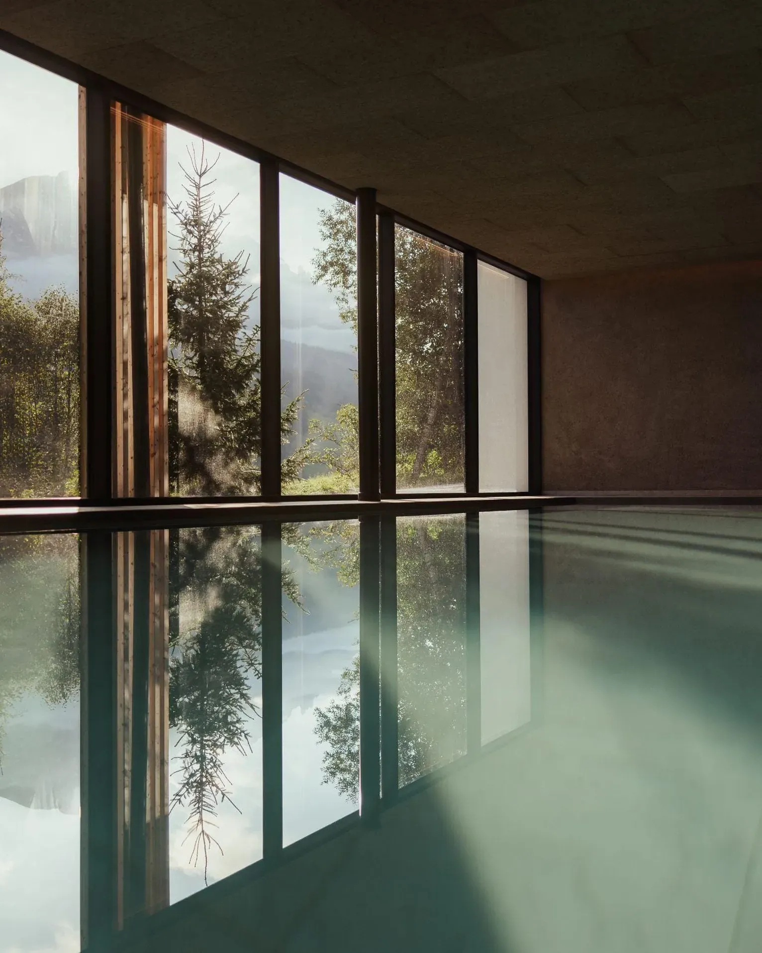 Indoor pool at the Hotel Lech da Sompunt, with large windows overlooking the lush greenery and the Dolomites, reflecting a soft natural light.