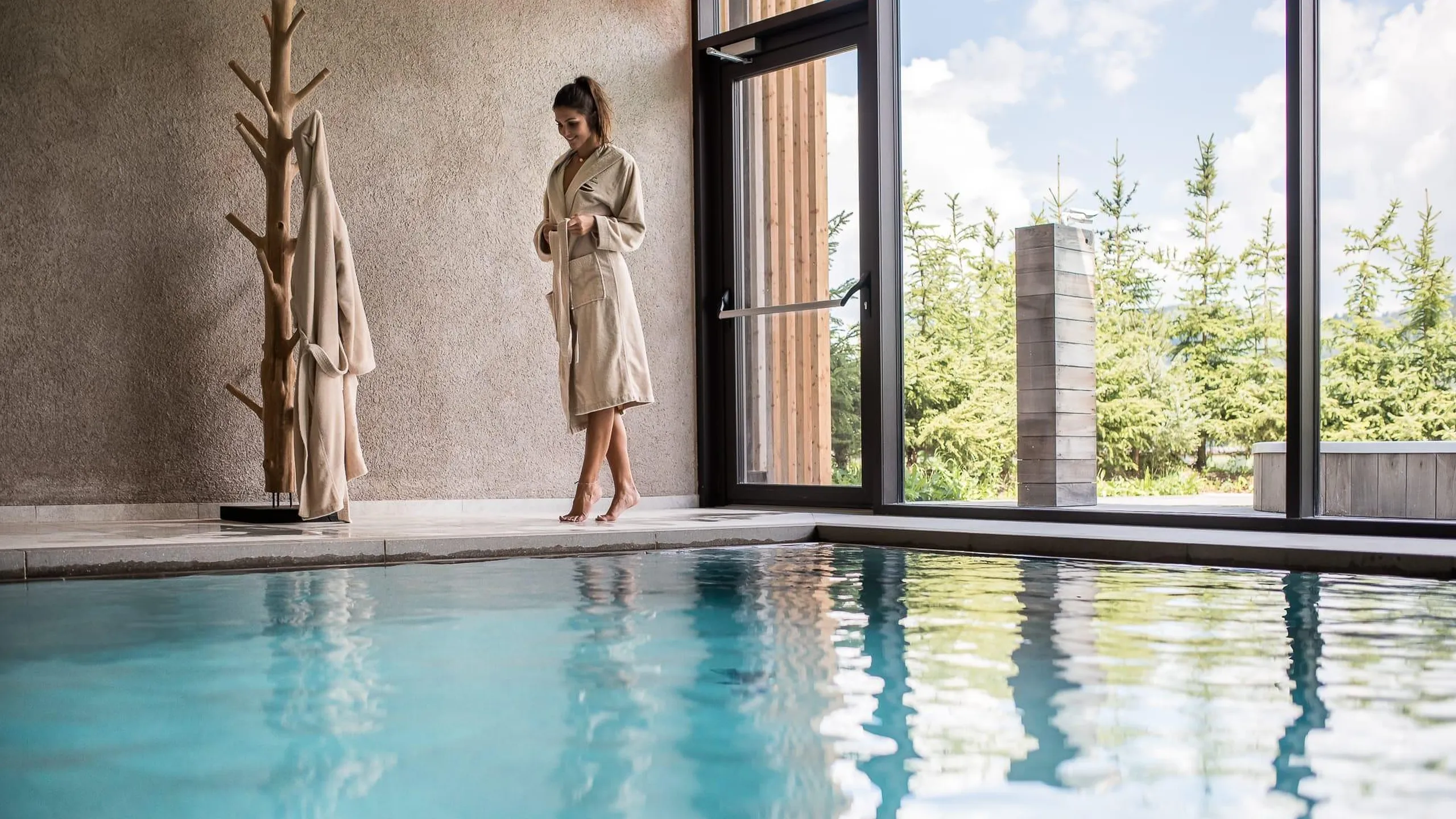 A woman in a beige robe stands beside the indoor pool of the Hotel Lech da Sompunt in Alta Badia.
