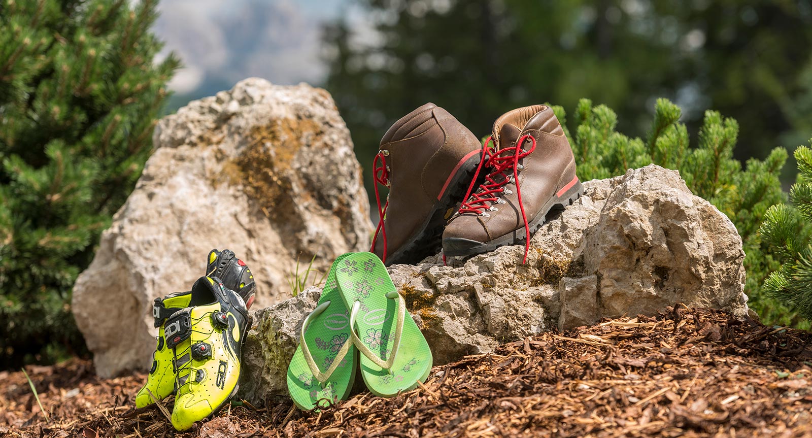 Cycling shoes, hiking shoes and flip flops placed outside next to a stone